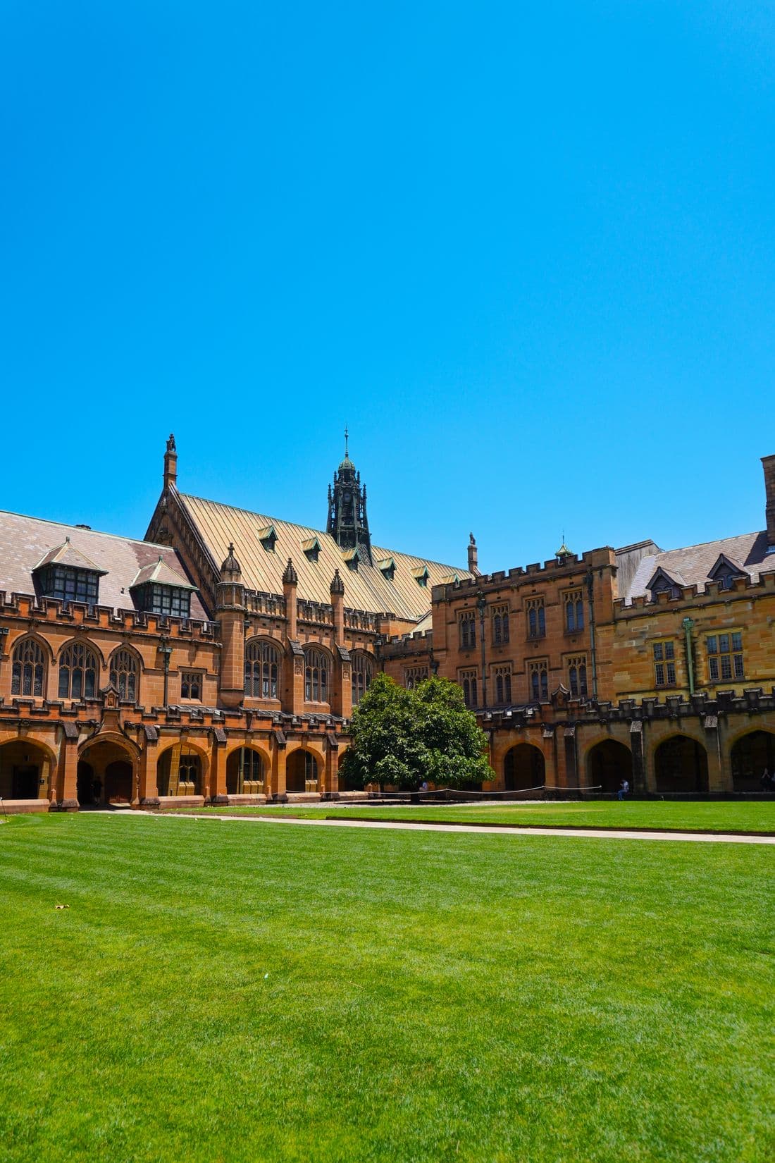 A historic university quadrangle with Gothic buildings around a lawn under a clear blue sky