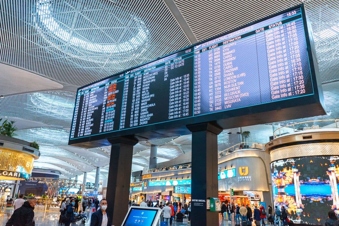 An airport departure board and passing travelers