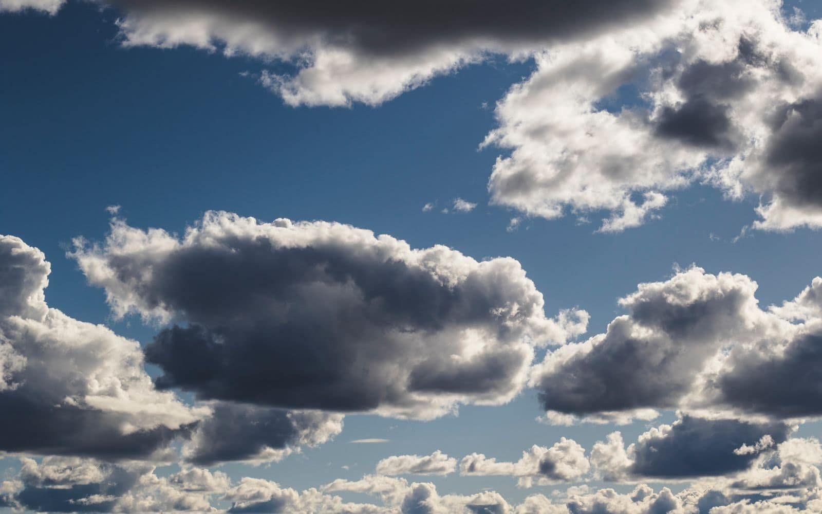 A bright daytime sky of soft white and grey cumulus clouds against blue, layered from horizon to overhead.