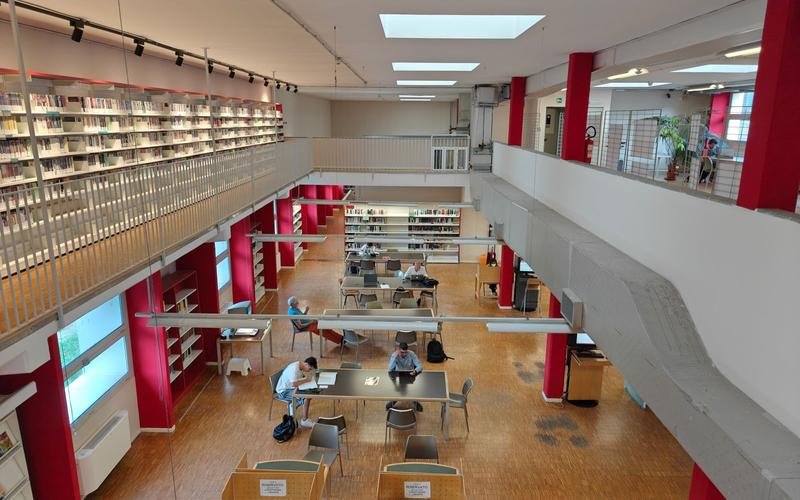 A two-level university library with bookshelves along a mezzanine and students at study tables
