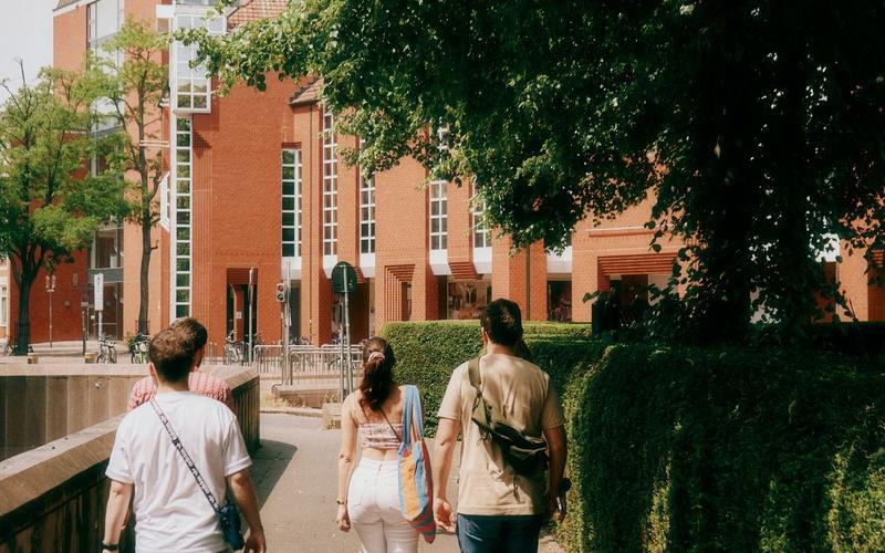 Three students walking a campus path toward a red-brick university building