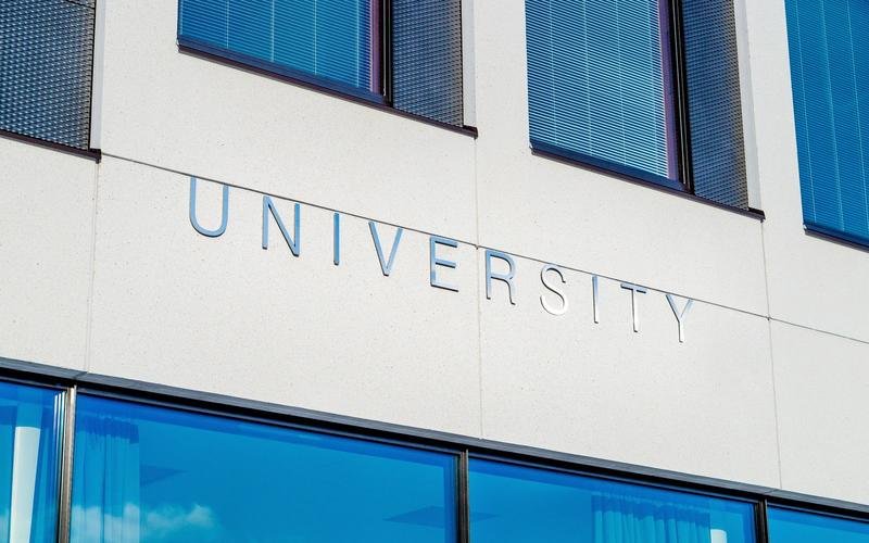 Metal UNIVERSITY lettering on a pale stone facade above blue-tinted windows